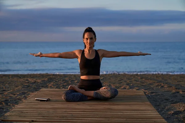 在靠近大海的海岸进行瑜伽训练时 身穿运动服的西班牙裔女性全身而退 双手张开 坐在帕吉萨那 — 图库照片