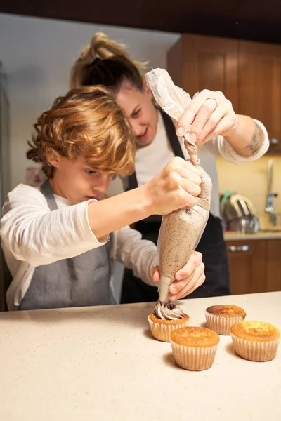 Stock vertical photo of a girl wearing an apron helping a boy to decorate cupcakes with a pastry bag