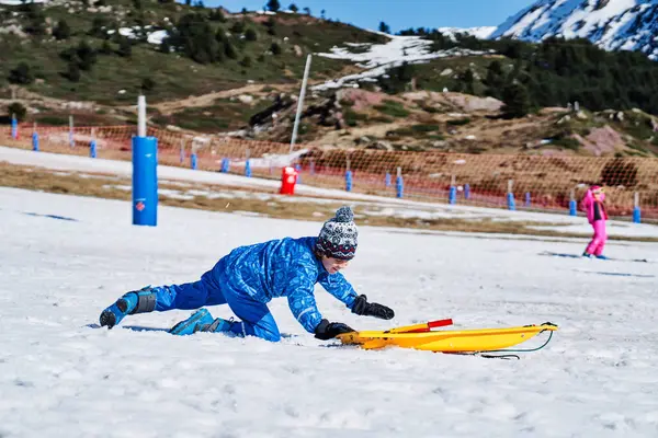 穿着蓝色外套 头戴一顶帽子的孩子爬上雪坡 爬上黄色塑料雪橇 在滑雪胜地玩乐的侧视图 — 图库照片