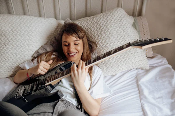 上から若いブルネットの女性がベッドの上でギターを弾く — ストック写真