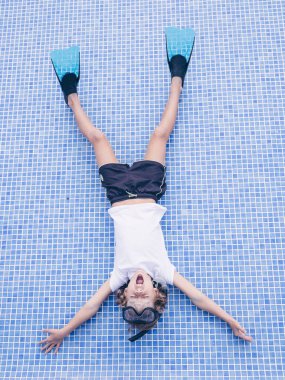 Dalış maskesi takmış, yüzgeçleri boş havuzun dibinde uzanmış ve yüksek sesle bağıran tüm vücudunun en üst görüntüsü.