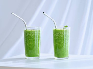 Açık arkaplanda beyaz arka planda duran pipetlerle sunulan detoks için sağlıklı yeşil smoothie ile şeffaf bardaklar