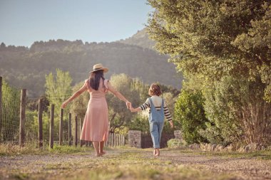 Güneşli bir günde, anne ve oğlunun çimenli çayırlarda el ele yürümeleri.
