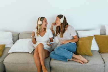 Hafif oturma odasındaki rahat koltukta kablosuz kulaklıkla müzik dinlerken akıllı telefonlu olumlu bayan arkadaşlar şarkı söylüyorlar.