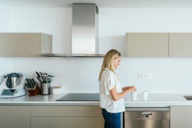 Kadın mutfak tezgahında çeşitli çatal bıçaklarla dikilirken beyaz bardaklarda çay yaparken modern apartmanda
