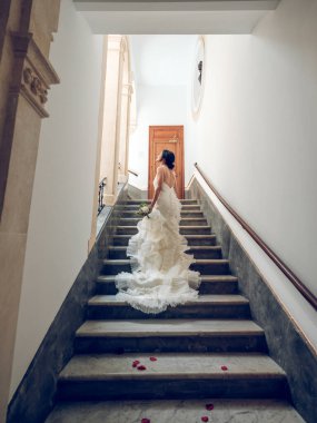 Arkadan bakıldığında, beyaz gelinlikli, fırfırlı ve dantelli tanımlanamayan gelin üst katta kırmızı gül yapraklarıyla yürüyordu ve hayaller kurarak pencereye bakıyordu.