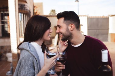 Yakışıklı bir adam ve güzel bir kadın terasta oturup güzel şarapların tadını çıkarırken gülümseyip birbirlerine bakıyorlar.