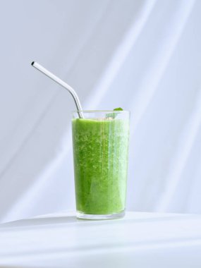 Modern ışık stüdyosunun beyaz arka planına saman konmuş lezzetli, sağlıklı, ferahlatıcı yeşil smoothie ile dolu bardak.