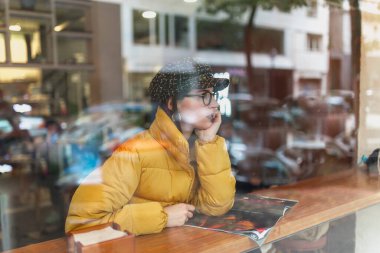 Moda dergilerindeki çekici genç bayanın yan görünüşü ve kafenin camının arkasında otururken bakışları.
