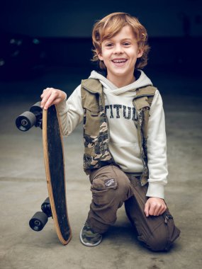 Şık giyinmiş, elinde kaykayla caddede beton zeminde oturmuş gülümseyen ve kameraya bakan bir sürü yakışıklı çocuk.