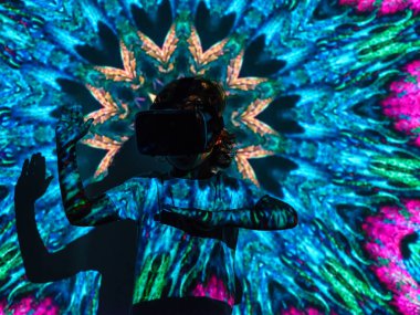 VR kulaklıklı anonim çocuk, parlak neon renkli projektör aydınlatması altında ellerini kaldırmış dururken sanal gerçeklikte oynuyor.