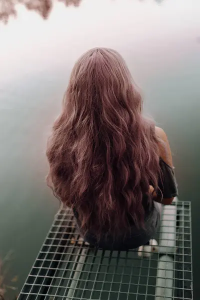 一个有着粉色头发的性感女人安安静静地坐在湖上的码头上 — 图库照片