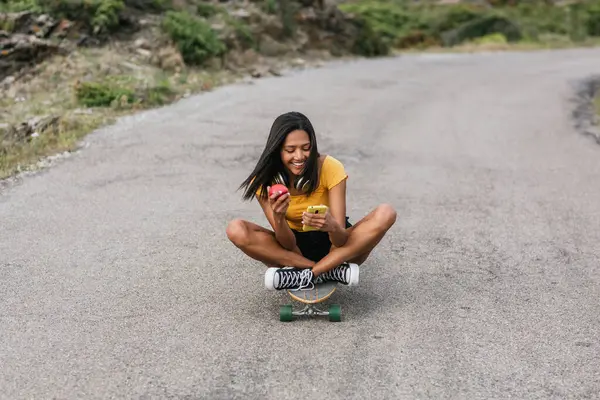 Etnisk Kvinna Surfa Smartphone Medan Sitter Longboard Asfalterad Väg — Stockfoto