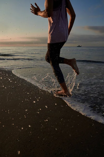 日落时分 在大自然的训练中 穿着运动服的匿名赤脚跑步者在潮湿的沙滩海岸上跑得很快 — 图库照片