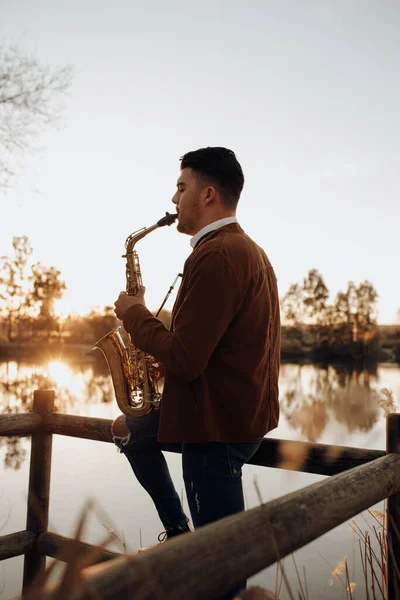 日落时在湖中演奏萨克斯风的年轻音乐家 — 图库照片