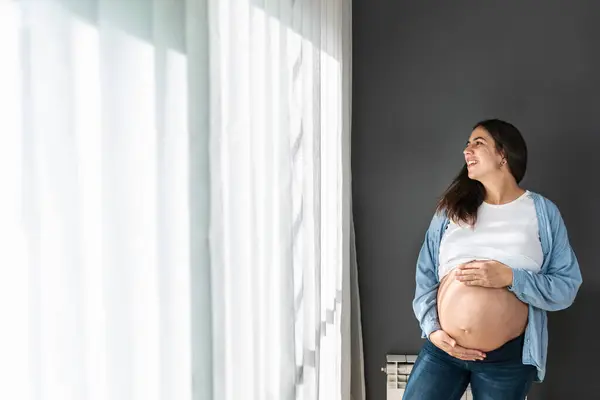Positive Pregnant Female Gently Touching Tummy While Standing Room Looking — Stok fotoğraf