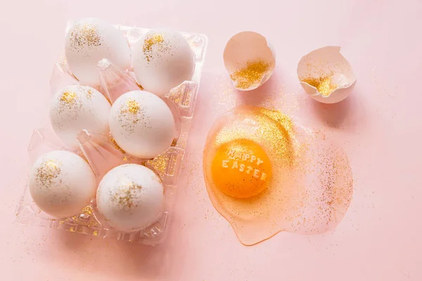 テキスト付き壊れた輝く卵のトップビューピンクの背景にプラスチック製の箱にハッピーイースターと生の卵 — ストック写真