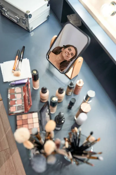 Güzellik Salonundaki Makyaj Malzemeleriyle Masada Otururken Aynaya Yansıyan Içerikli Bayan — Stok fotoğraf