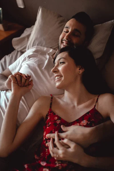 快適なベッドの上で一緒に寝そべっている間に美しい女性を笑顔と抱擁上から — ストック写真