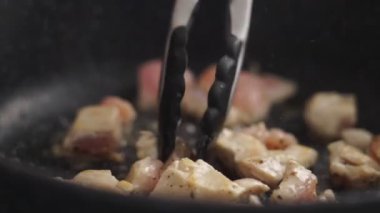 Yüksek açılı yakın çekim. Mutfak maşası parçaları tavada kızarırken isimsiz birinin gerçek zamanlı görüntüsü.