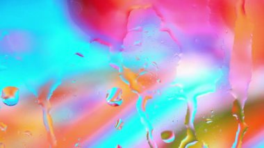 Renkli su penceresinden çok renkli arka planda yağmur damlalarıyla birlikte cam yüzeyine yayılıyor.