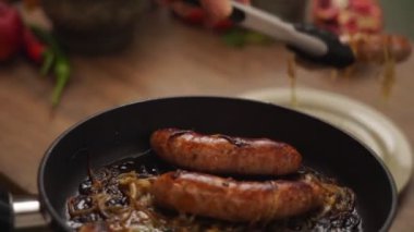 Gerçek zamanlı anonim aşçı ev yapımı kızarmış sosis ve mutfak maşası ile soğan koyar.