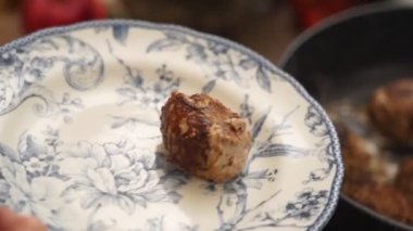 Yüksek açılı, gerçek zamanlı, anonim bir insan mutfak maşasıyla tavadan pirzola alıyor ve tabağa koyuyor.