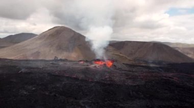 İzlanda 'da dumanla çevrili volkanik dağ zirvesinden fışkıran sıcak turuncu lavlar.