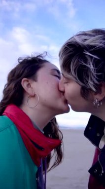 Dış giysili genç eşcinsel çiftin yan görünüşü Battaniyenin üzerinde oturuyor ve nazikçe öpüşüyorlar