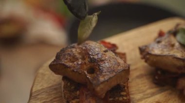 Yakın çekim yüksek açı. Anonim kişi, arka planda bulanık arka planda kesilmiş defne yapraklarıyla kızartılmış et parçalarını dekore ediyor.