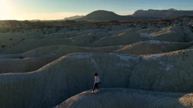 Gün batımında çölde fotoğraf çekilirken kaba kayalık oluşum üzerinde duran tanınmayan bir yolcunun robot görüntüsü.