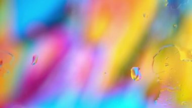 Renkli su penceresinden çok renkli arka planda yağmur damlalarıyla birlikte cam yüzeyine yayılıyor.