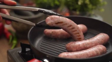 Gerçek zamanlı anonim aşçı ev yapımı sosisleri pişiriyor. Mutfak maşaları elektrikli ocağa yerleştirilmiş.