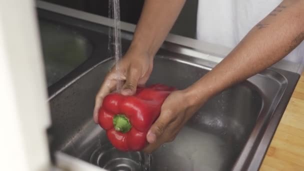 キッチンで健康的なサラダを調理しながら 水流でシンクで新鮮なベルペッパーを洗う認識できないアフリカ系アメリカ人の男性 — ストック動画