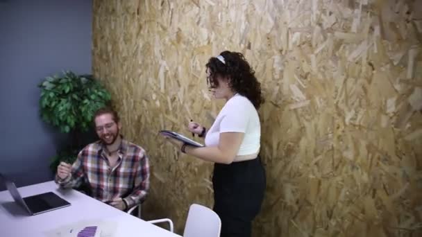 オフィスのプロジェクトで協力しながら 女性同僚とラップトップに座っているテーブルに座っているチェッカーされたシャツのポジティブなひげ付き男 — ストック動画