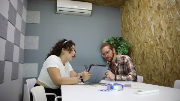 オフィスのプロジェクトで協力しながら タブレットを使用して女性同僚とラップトップに座っているメガネ付きのチェッカーされたシャツのひげ付き男 — ストック動画