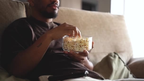 周末与遥控器一起睡在舒适的沙发上 一边吃爆米花一边看电视的非洲裔美国男性 — 图库视频影像