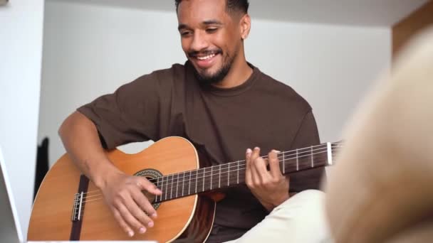 배경에 편안한 소파에 기타를 노트북에 비디오 자습서를 긍정적인 아프리카계 음악가 — 비디오