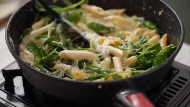 フライパンにほうれん草とクリームと黒いスパチュラマカロニパスタとチーズで攪拌する匿名料理の高角度リアルタイム — ストック動画