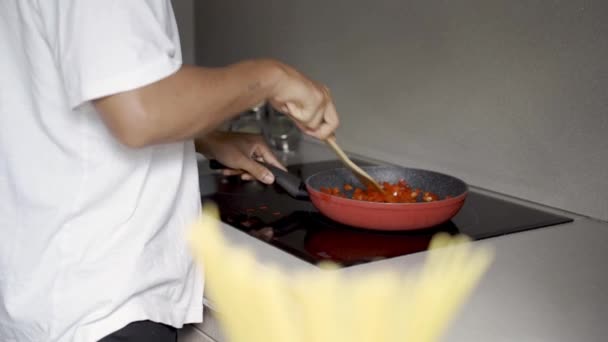 キッチンの調理プロセス中に鍋にトマトを揚げながらおいしい料理を準備している 認識できない民族男性の側面のビュー — ストック動画