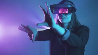 Uzamış kollu, VR kulaklık takan tanınmayan bir kadın, projektör aydınlatmasıyla duvarın yanındaki mavi neon ışığı altında sanal gerçekliği keşfediyor.