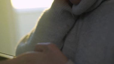 Sıcak örgü kazaklı, akıllı telefonlara bakıp pencerenin yanında duran dalgın bir kadın.