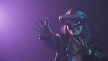 Uzamış kollu, VR kulaklık takan tanınmayan bir kadın, projektör aydınlatmasıyla duvarın yanındaki mavi neon ışığı altında sanal gerçekliği keşfediyor.