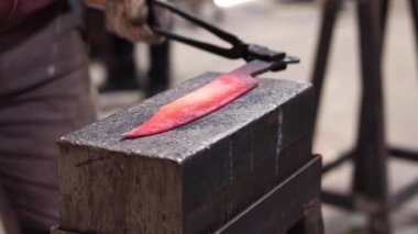 Eldivenli anonim bir zanaatkarın demirci atölyesinde çekici ile sıcak metal detayı yaparken çekilmiş görüntüler.