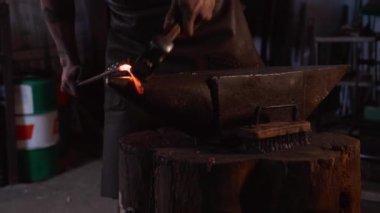 Geleneksel demircilikte çalışırken genç ve vahşi zanaatkârın apron ısıtma ve örse çekiçle vuruşunun yan görüntüsü