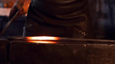 Elinde çekiçle örsün yanında çalışan kimliği belirsiz genç bir erkek.