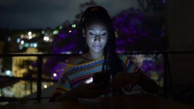 Afrika kökenli Amerikalı kadın akşamları sokak kafesinde oturuyor ve hafta sonunun keyfini çıkarırken sosyal medyada mesajlaşıyor.