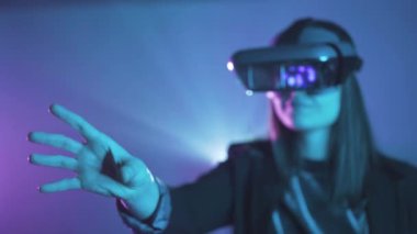 Uzamış kollu, VR kulaklık takan, projektör ışıklandırmasıyla duvarın yanındaki mavi neon ışığı altında sanal gerçekliği keşfeden tanınmamış bir kadının yan görüntüsü.