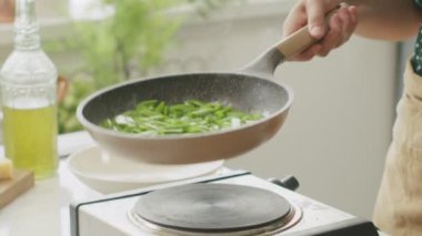 Gündüz vakti mutfakta sağlıklı bir akşam yemeği hazırlarken tavada taze taze taze fasulye karıştıran isimsiz bir adamın tepesinden.