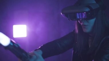 Uzamış kollu, VR kulaklık takan tanınmayan bir kadın, projektör aydınlatmasıyla duvarın yanındaki mavi neon ışığı altında sanal gerçekliği keşfediyor.